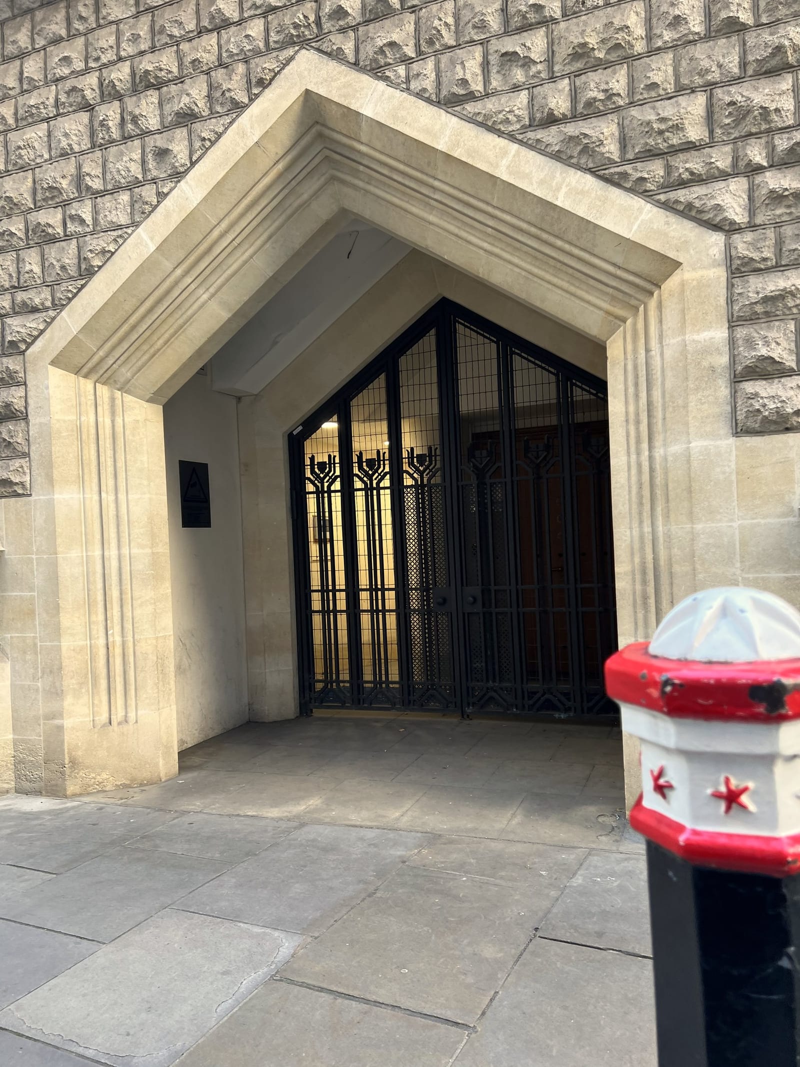 A pointed stone doorway with ornate black iron gates and a City of London bollard